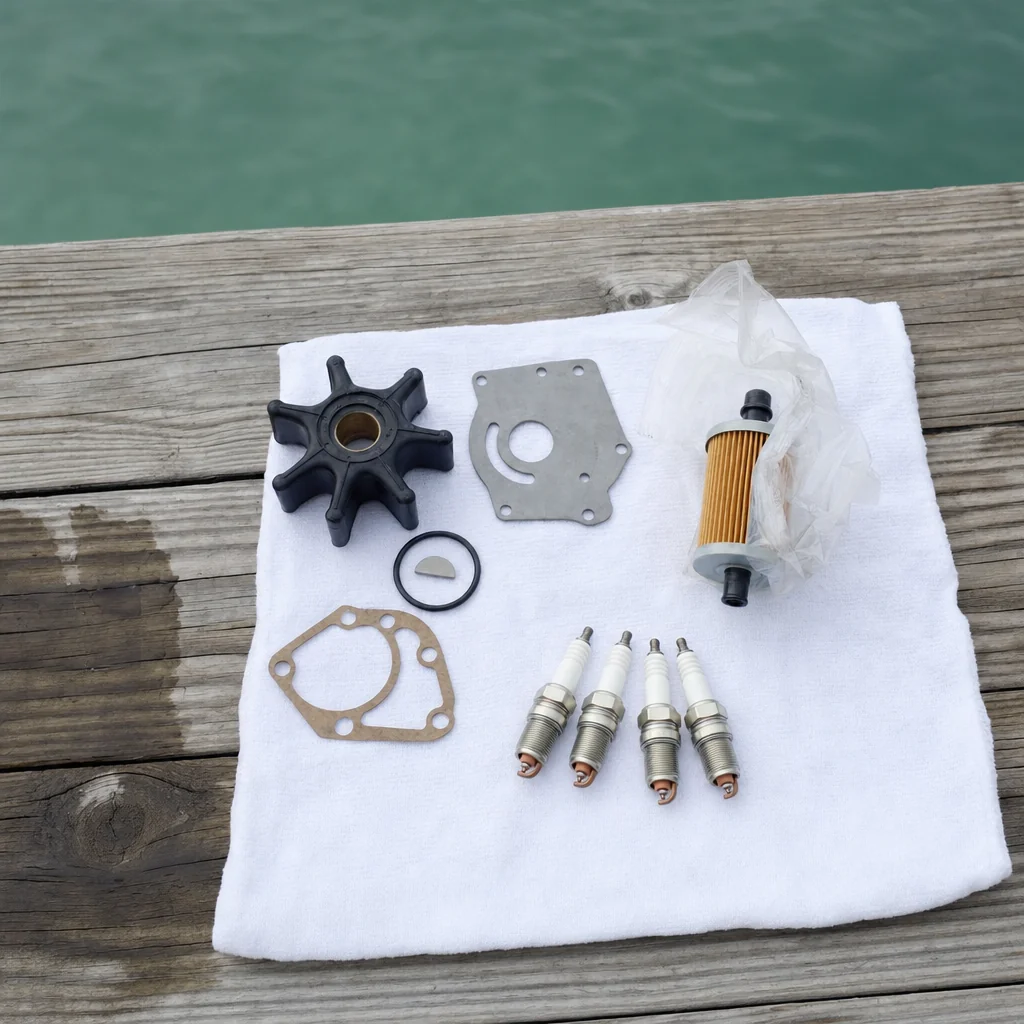 Marine engine service parts laid out on white cloth at Stuart dock, including impeller, gasket, filter, and spark plugs.
